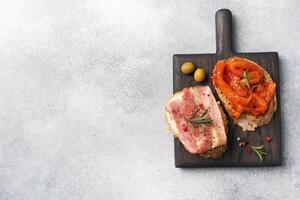 Whole grain bread sandwiches with cream cheese, bacon and canned peppers with tomato on a wooden cutting Board. Gray concrete background with Copy space. photo