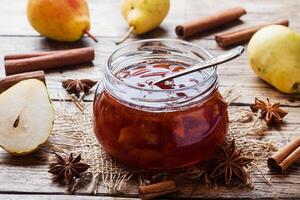 Homemade pear jam in a jar and fresh pears on a wooden background. photo