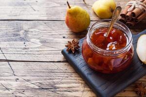 Homemade pear jam in a jar and fresh pears on a wooden background. Copy space. photo