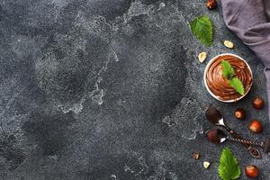 Nougat nut chocolate in a plate on a dark concrete background with hazelnut nuts. Concept of Breakfast. Copy space. photo