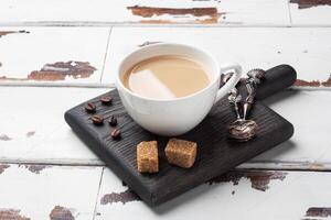A Cup of coffee with milk and cubes of cane sugar on a wooden stand. Background of white rustic boards. Copy space. photo