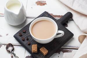 A Cup of coffee with milk and cubes of cane sugar on a wooden stand. Background of white rustic boards. Copy space. photo
