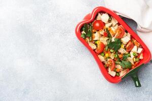 Stewed chicken meat with vegetables carrots peppers peas corn in a plate in the form of red pepper. Copy space. photo
