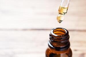 Drop falls from the pipette. Bottle of cosmetic oil with a pipette on a wooden background. Copy space. Selective focus. photo