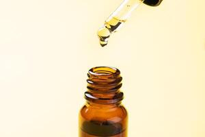 Drop falls from the pipette. Bottle of cosmetic oil with a pipette on a yellow background. Copy space. Selective focus. photo