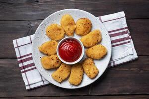 Fried chicken nuggets with tomato ketchup sauce. Wooden background. Copy space. photo