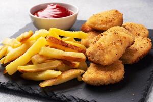 Fried potatoes and chicken nuggets with tomato ketchup sauce. Fast food concept of unhealthy food. Grey concrete table Copy space. photo