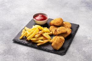 Fried potatoes and chicken nuggets with tomato ketchup sauce. Fast food concept of unhealthy food. Grey concrete table Copy space. photo