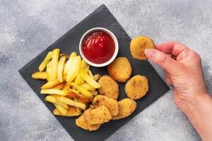 Fried potatoes and chicken nuggets with tomato ketchup sauce. Fast food concept of unhealthy food. Grey concrete table Copy space. photo