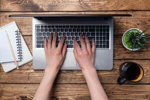 Working wooden table at home or in the office. Computer laptop coffee cactus. Flat lay conceptions Woman working at computer hands. photo
