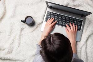 Woman lying on a white wool blanket and working at computer hands. Concept of working and learning at home. Copy space. photo