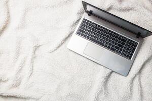 Notebook Computer lying on a white wool blanket. Concept of working and learning at home. Copy space. photo