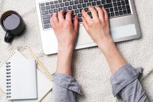 Woman lying on a white wool blanket and working at computer hands. Concept of working and learning at home. Copy space. photo