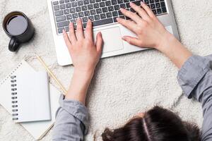 Woman lying on a white wool blanket and working at computer hands. Concept of working and learning at home. Copy space. photo