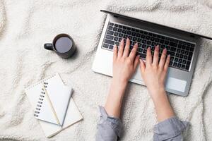 Woman lying on a white wool blanket and working at computer hands. Concept of working and learning at home. Copy space. photo