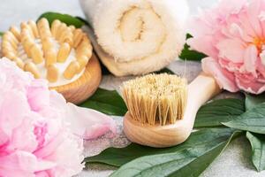 Concept SPA and Wellness. Massage brush, cosmetic oils and soap. Light background with peony flowers. photo