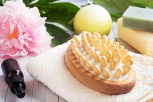 Concept SPA and Wellness. Massage brush, cosmetic oils and soap. Light background with peony flowers. photo