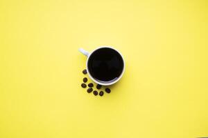 Black coffee in a Cup and coffee beans on a yellow background. Top view Copy space. photo