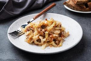 Stewed cabbage with meat on a plate. Dark concrete background. photo