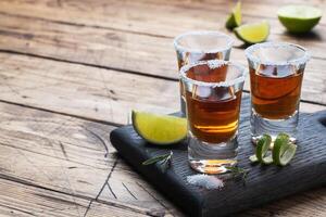 vaso con alcohol, sal y Lima en un de madera antecedentes. coñac whisky tequila. el concepto de el fiesta. selectivo atención Copiar espacio. foto