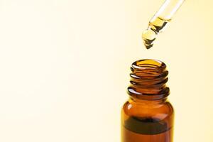 Drop falls from the pipette. Bottle of cosmetic oil with a pipette on a yellow background. Copy space. Selective focus. photo