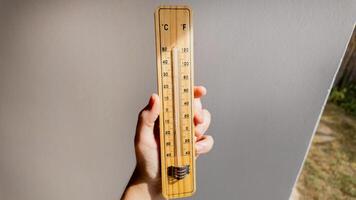 A hand holding a wooden thermometer indicates rising temperatures, highlighting concerns about global warming and climate change effects photo