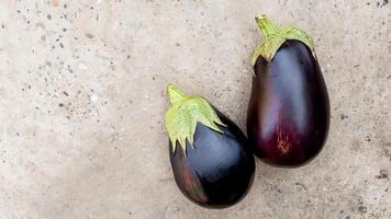 Two fresh eggplants on a speckled concrete surface representing healthy cooking and vegetarian diet concepts photo