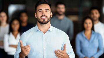 Charismatic male leader giving a presentation gesturing towards a digital screen diverse team in the background photo