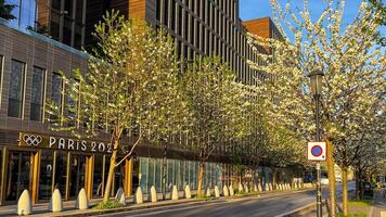 Blooming trees line a street next to a building with Paris 2024 signage, symbolizing preparation for the Olympics photo