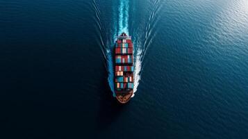 Aerial shot of a cargo ship filled with multi colored containers cruising through calm ocean waters sunlight reflecting off the surface as it creates a wide wake photo