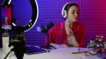 Woman beauty blogger streaming a vlog from studio and showing new brushes. Online content creator applying a makeup on video