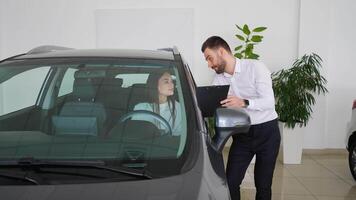 Car salesman standing at the dealership telling about the features of the car to the customers. Buying their first car together video