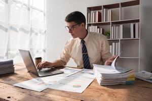 Businessman Working in Modern Office with Documents and Laptop, Analyzing Data and Reports, Professional Workspace, Daylight through Windows, Focused and Productive Work Environment photo