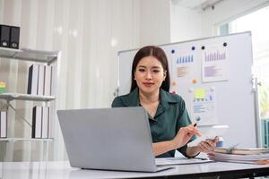 Young Accountant Analyzing Financial Documents on Laptop in Modern Office Setting with Charts and Graphs in Background photo