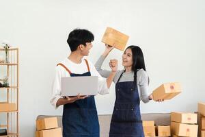 Happy Couple Running a Small Online Business from Home, Celebrating Success with Laptops and Package, E-commerce Entrepreneurs in Casual Clothing, Modern Home Office Environment photo