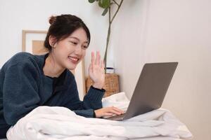 Relaxed Young Woman Using Laptop in Cozy Home Setting, Smiling and Waving, Casual Lifestyle, Remote Work or Online Communication photo