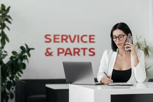 Sales woman use smartphone, have business call at car showroom. Car dealership client service and parts. Business Process and Problem Solving, Quality Control. Cell phone advise to choose, buy auto photo