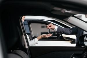 Hand holding car key remote, with modern car background. A car dealer hands over new car key to cheerful caucasian woman, indicative of a new purchase in a showroom. Rent, credit, insurance photo