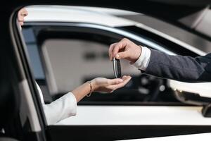 Man in front of the new car and holding keys. Salesman is carrying the car keys delivered to the customer at the showroom. Car key handover concept. Female bought herself a beautiful new car. photo