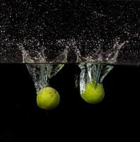 Two apples are falling into water with water splashing on them photo