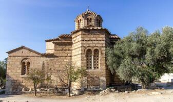 Ancient Byzantine-style stone church with domed roof and cross on top, surrounded by trees and path in Athens, Greece. Outdoor architectural photography photo