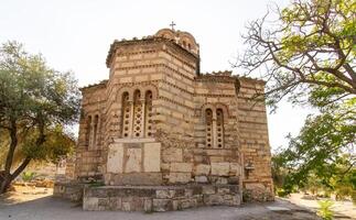Ancient Byzantine-style stone church with domed roof and cross on top, surrounded by trees and path in Athens, Greece. Outdoor architectural photography photo