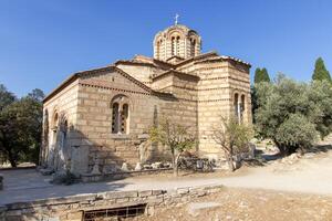 Ancient Byzantine-style stone church with domed roof and cross on top, surrounded by trees and path in Athens, Greece. Outdoor architectural photography photo
