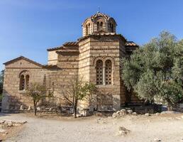 Ancient Byzantine-style stone church with domed roof and cross on top, surrounded by trees and path in Athens, Greece. Outdoor architectural photography photo