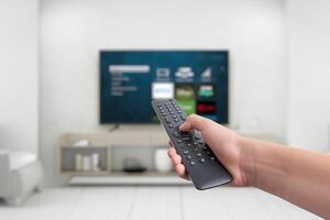 Hand holding a remote control for a smart TV, featuring app buttons for streaming services. Concept of versatile entertainment, showcasing the functionality of smart TVs for various photo