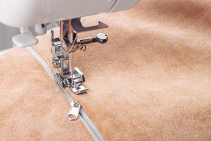 Modern sewing machine special presser foot with beige fabric and zipper, closeup photo