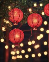 A string of red Chinese lanterns hanging against a night sky, with glowing golden fairy lights in the background, warm festive atmosphere. photo