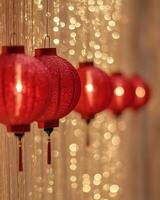 A row of glowing red lanterns hanging in soft lighting, with golden sparkles in the blurred background, creating a warm festive tone. photo