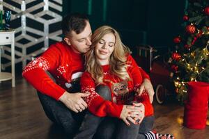 A charming couple in love in traditional Christmas red sweaters spend time near the Christmas tree photo