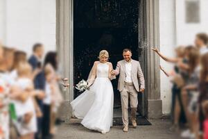 Smiling and happy young married couple leaving church after marriage. Launch of confetti, confetti and flower petals that are good wishes for marriage. photo
